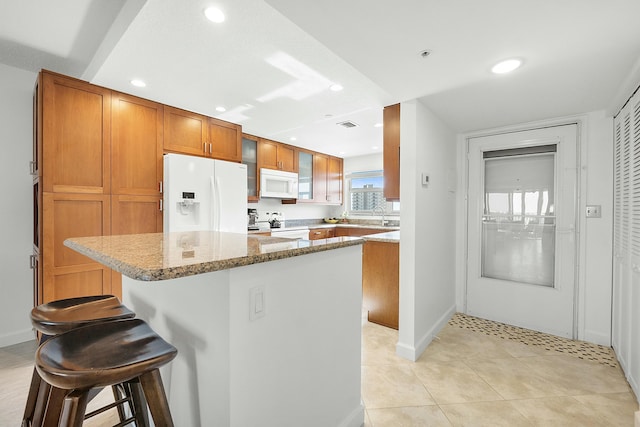 kitchen featuring white appliances, light stone countertops, a breakfast bar, glass insert cabinets, and brown cabinets