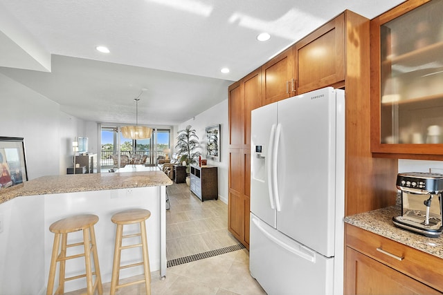 kitchen with brown cabinetry, light tile patterned floors, white refrigerator with ice dispenser, and glass insert cabinets