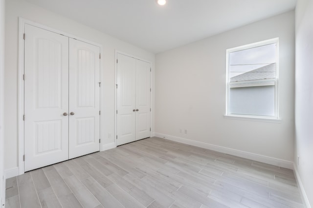 unfurnished bedroom with light wood-type flooring, baseboards, and two closets