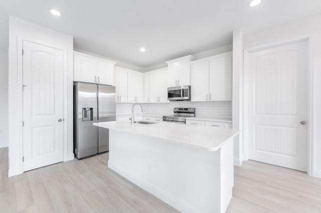 kitchen with a center island with sink, light wood-style flooring, appliances with stainless steel finishes, white cabinetry, and a sink