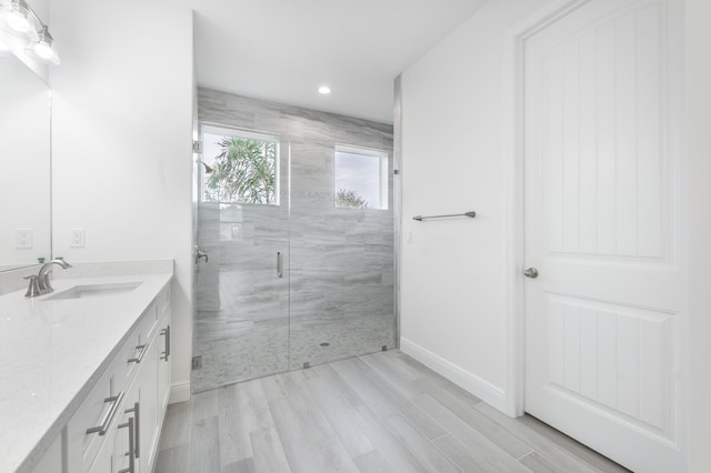 bathroom featuring vanity, wood finished floors, baseboards, and a marble finish shower