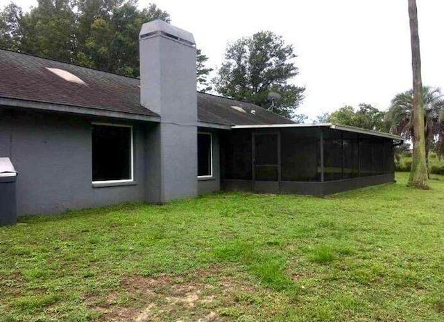 rear view of property with a yard, stucco siding, a chimney, and a sunroom