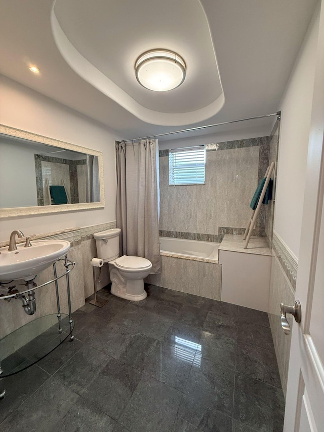 full bathroom with a raised ceiling, toilet, tiled shower / bath, and a sink