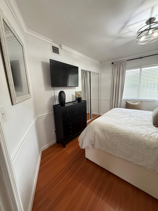 bedroom with crown molding, wood finished floors, visible vents, and baseboards