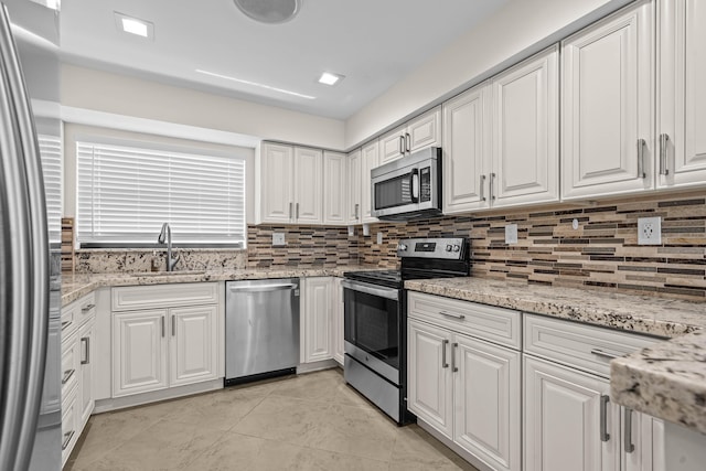 kitchen with light stone countertops, decorative backsplash, appliances with stainless steel finishes, white cabinetry, and a sink