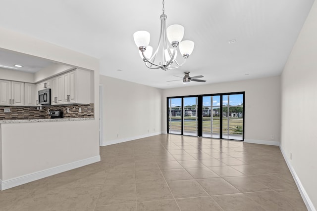 interior space with light tile patterned floors, ceiling fan with notable chandelier, and baseboards