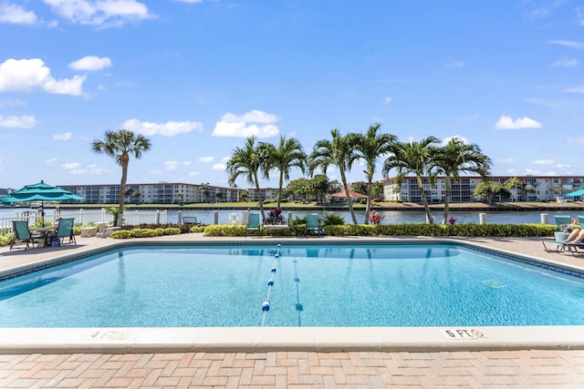 community pool with a patio, fence, and a water view