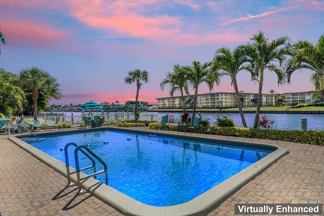 pool at dusk featuring a patio area, fence, a community pool, and a water view