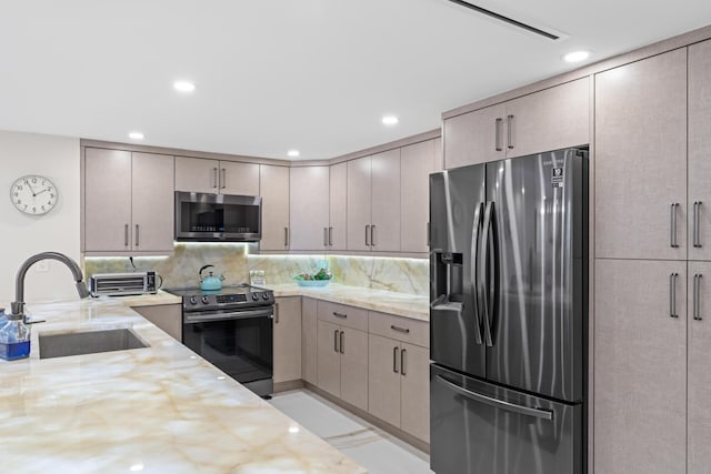 kitchen with a sink, light stone countertops, backsplash, and appliances with stainless steel finishes