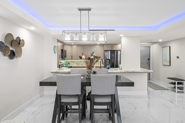 dining area featuring marble finish floor, a raised ceiling, and baseboards