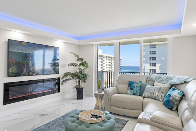 living room with a glass covered fireplace, marble finish floor, and a tray ceiling