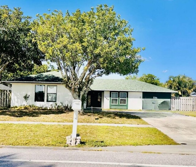 ranch-style home with concrete driveway, fence, a front yard, and stucco siding