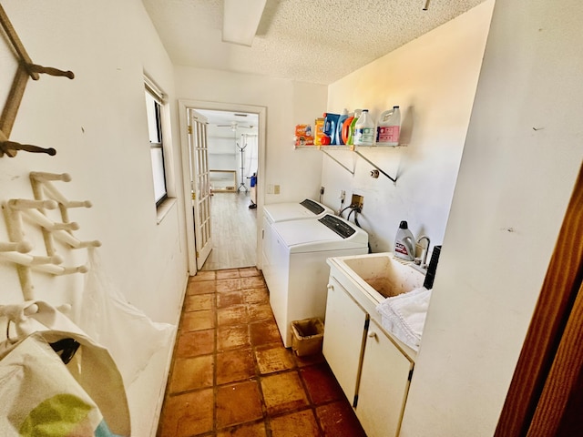 washroom featuring a textured ceiling, cabinet space, a sink, and washing machine and clothes dryer