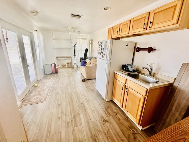 kitchen featuring visible vents, light wood-style flooring, a sink, freestanding refrigerator, and light countertops