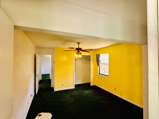 interior space featuring dark colored carpet, a ceiling fan, and baseboards