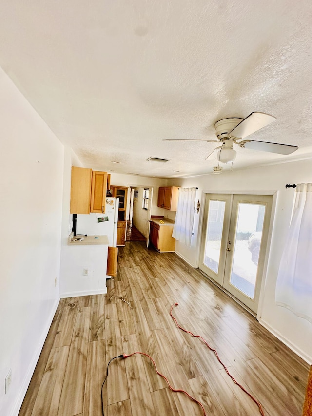 unfurnished living room with ceiling fan, a textured ceiling, french doors, light wood-type flooring, and visible vents