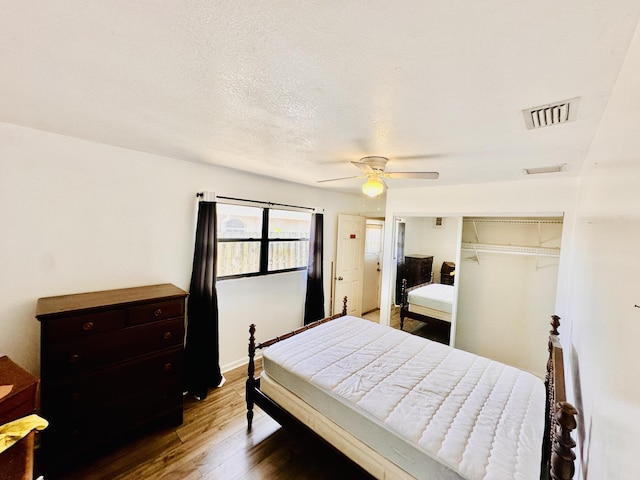 bedroom featuring ceiling fan, visible vents, wood finished floors, baseboards, and a closet