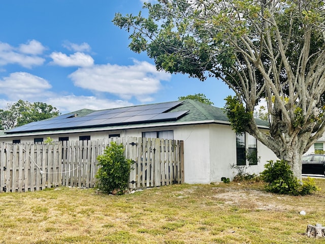 view of property exterior featuring a yard, a fenced front yard, roof mounted solar panels, and stucco siding