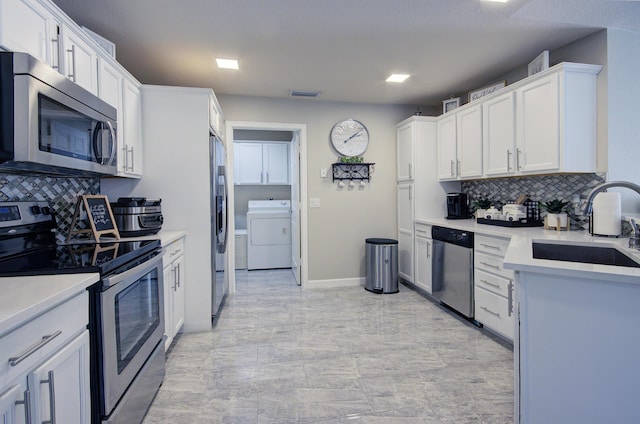 kitchen featuring washer / dryer, a sink, stainless steel appliances, light countertops, and white cabinetry