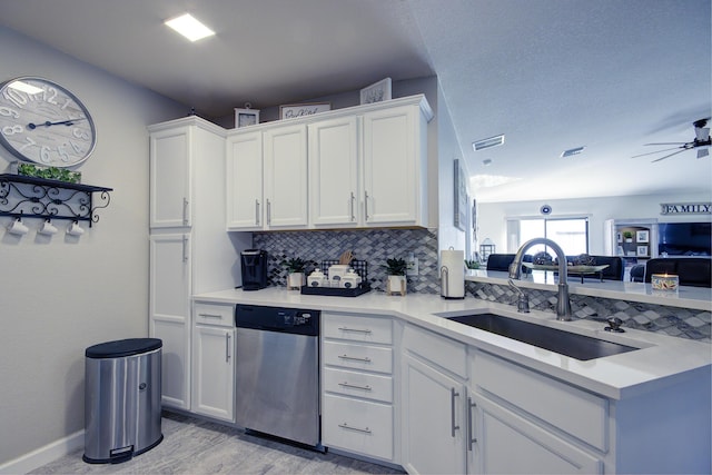 kitchen featuring a sink, stainless steel dishwasher, white cabinets, light countertops, and decorative backsplash