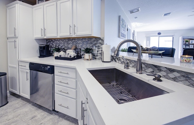 kitchen with visible vents, white cabinetry, a sink, dishwasher, and backsplash