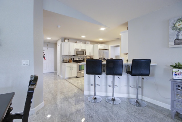 kitchen with baseboards, a kitchen bar, decorative backsplash, appliances with stainless steel finishes, and white cabinets