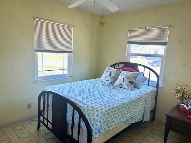 bedroom featuring a ceiling fan, baseboards, wallpapered walls, a textured ceiling, and tile patterned floors