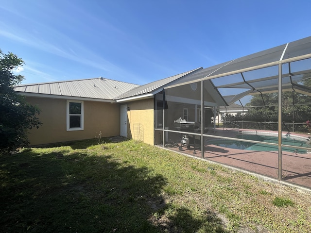 rear view of house with stucco siding, a patio, a yard, metal roof, and a lanai