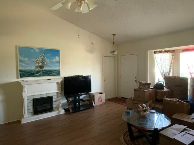 living area with a fireplace with raised hearth, a ceiling fan, a textured ceiling, wood finished floors, and vaulted ceiling