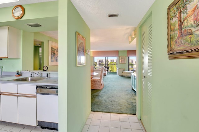 hallway with light carpet, light tile patterned floors, visible vents, and a sink