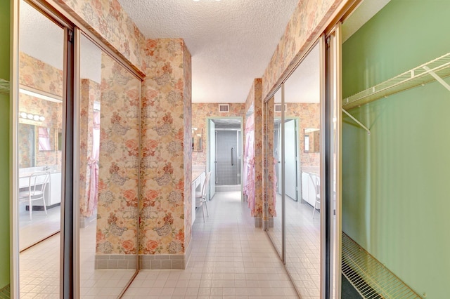 corridor featuring light tile patterned floors, visible vents, a textured ceiling, and wallpapered walls