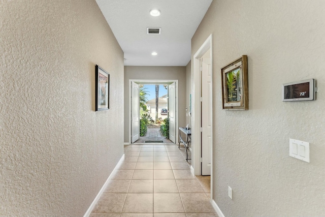 hall with light tile patterned floors, visible vents, baseboards, and a textured wall