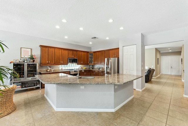 kitchen with visible vents, a sink, light stone counters, stainless steel appliances, and a large island with sink