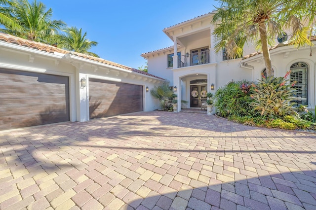 mediterranean / spanish-style house with a tile roof, stucco siding, decorative driveway, a balcony, and an attached garage