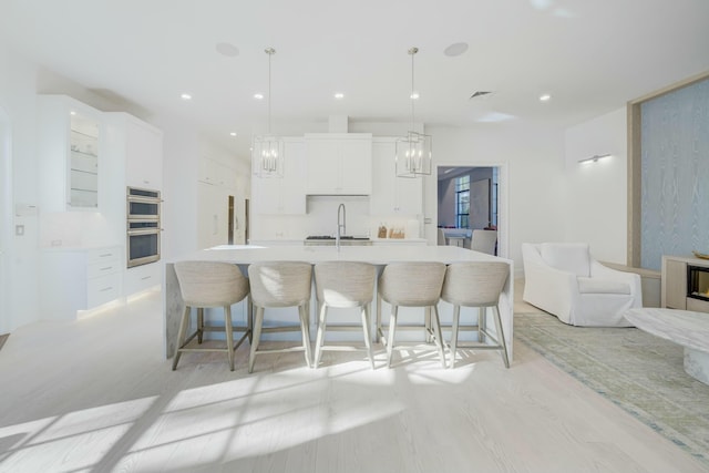 kitchen with a kitchen breakfast bar, a spacious island, double oven, white cabinets, and light countertops