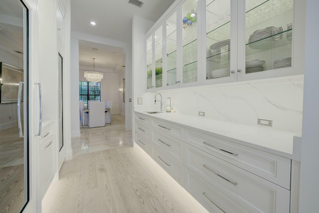 interior space featuring tasteful backsplash, visible vents, a chandelier, light wood-style floors, and a sink