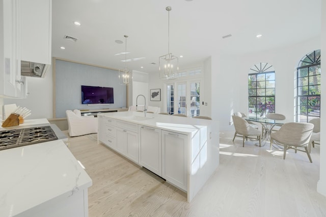 kitchen with visible vents, light wood-type flooring, a sink, open floor plan, and white cabinets