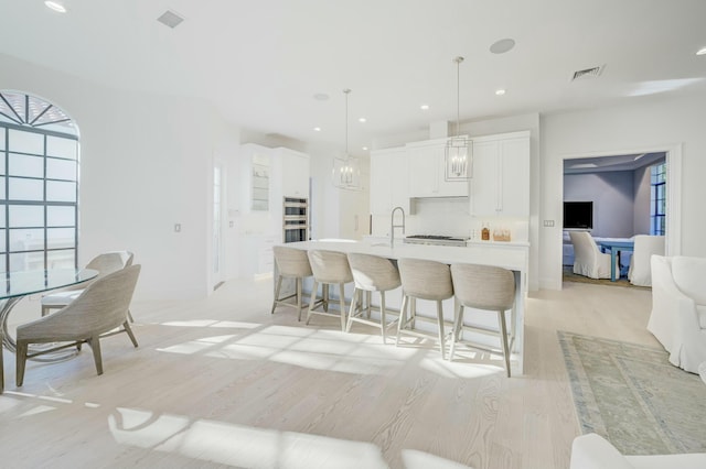 kitchen with light wood finished floors, visible vents, a center island with sink, a breakfast bar, and light countertops