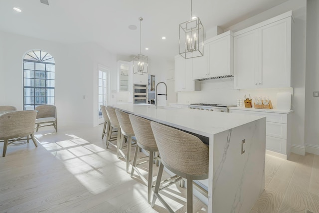 kitchen with a large island, double wall oven, a sink, white cabinetry, and light wood finished floors