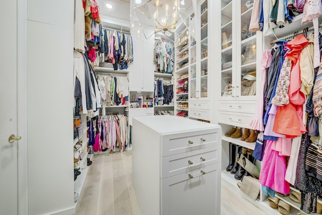 walk in closet with light wood-style floors and an inviting chandelier