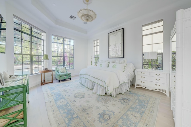 bedroom featuring a tray ceiling, visible vents, baseboards, and wood finished floors