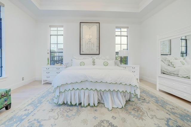 bedroom with baseboards, a raised ceiling, light wood-style floors, and ornamental molding