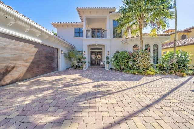 mediterranean / spanish-style house with a balcony, stucco siding, french doors, a garage, and decorative driveway