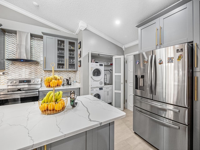 7882 Lake Sands Dr, Delray Beach, FL 33446 - kitchen featuring gray cabinetry, wall chimney range hood, lofted ceiling, stacked washer and dryer, and appliances with stainless steel finishes