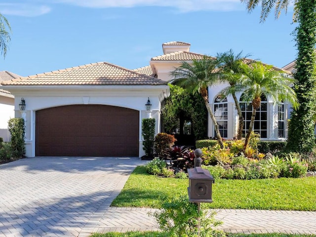 mediterranean / spanish house with stucco siding, decorative driveway, a garage, and a tiled roof