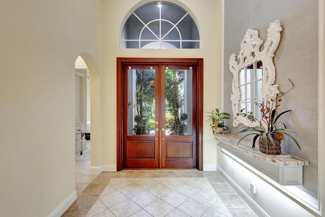 foyer featuring baseboards, french doors, a towering ceiling, light tile patterned flooring, and arched walkways