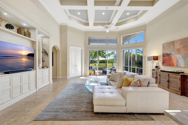 living area with built in shelves, a towering ceiling, arched walkways, coffered ceiling, and a ceiling fan