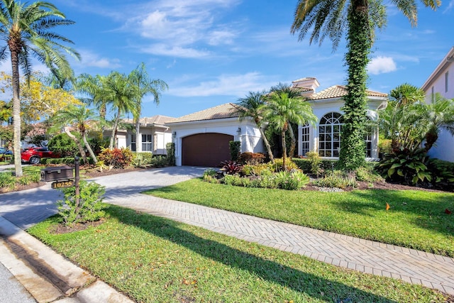 mediterranean / spanish home featuring a tiled roof, a front yard, stucco siding, driveway, and an attached garage