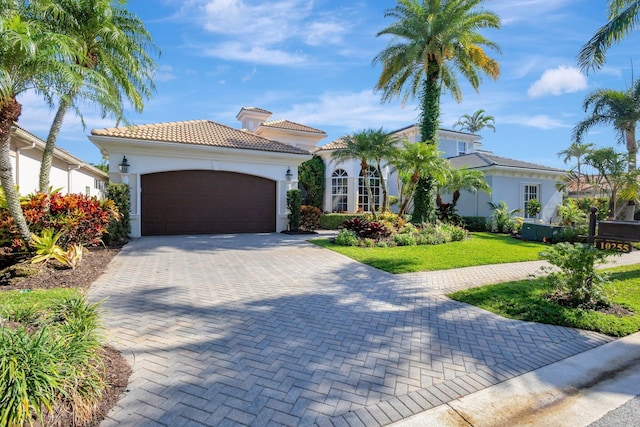 mediterranean / spanish house with a front yard, driveway, stucco siding, a garage, and a tiled roof