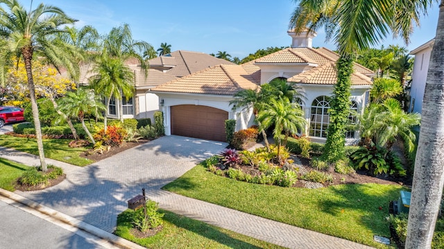 mediterranean / spanish house with stucco siding, decorative driveway, a front yard, an attached garage, and a tiled roof